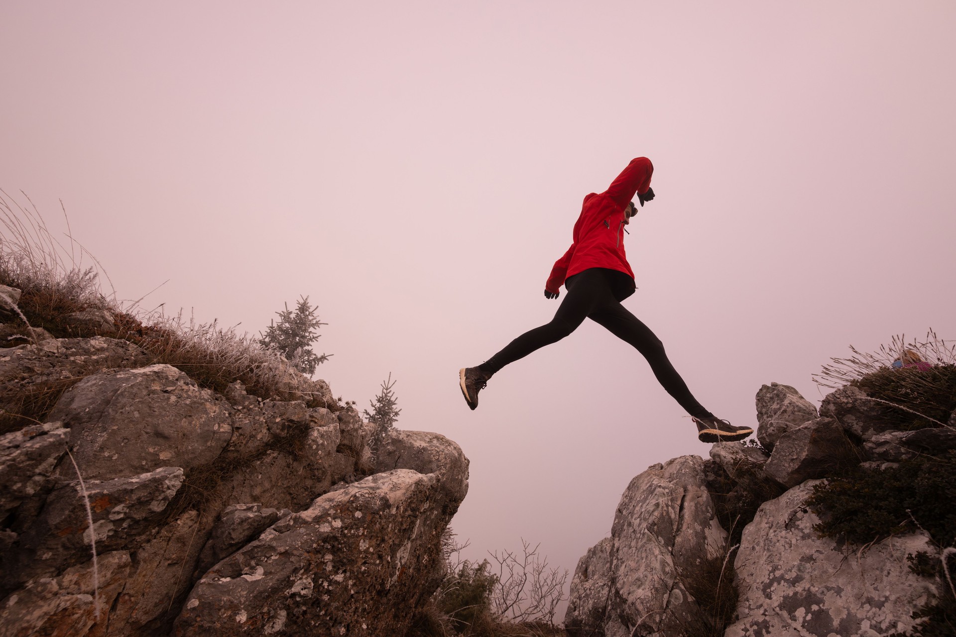 silhouette of a fitness man trail runner jumping over a cliff and running to a rocky mountain top in the early morning